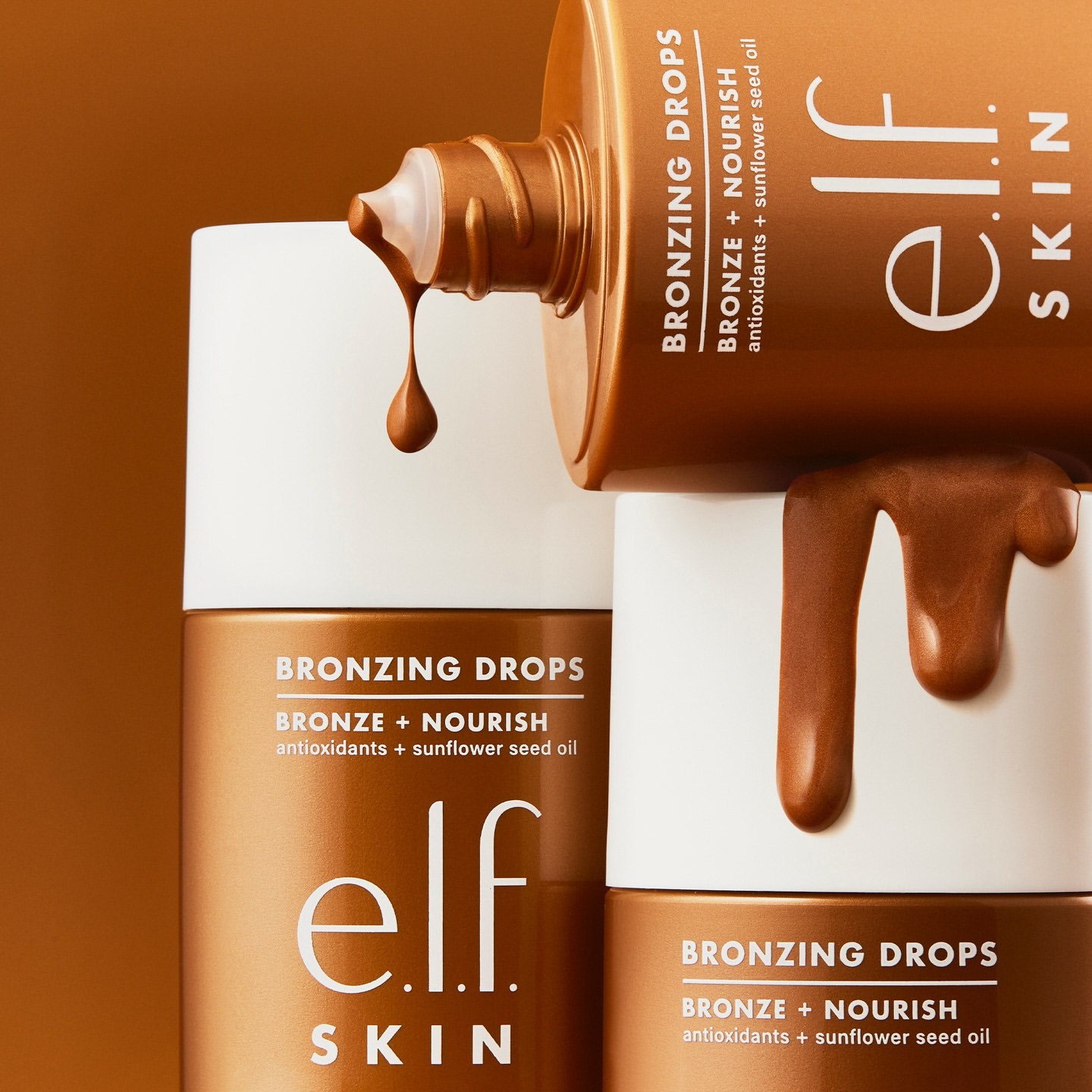Close-up of e.l.f. SKIN bronzing drops being poured from a bottle, product names visible, against a bronze-toned background.