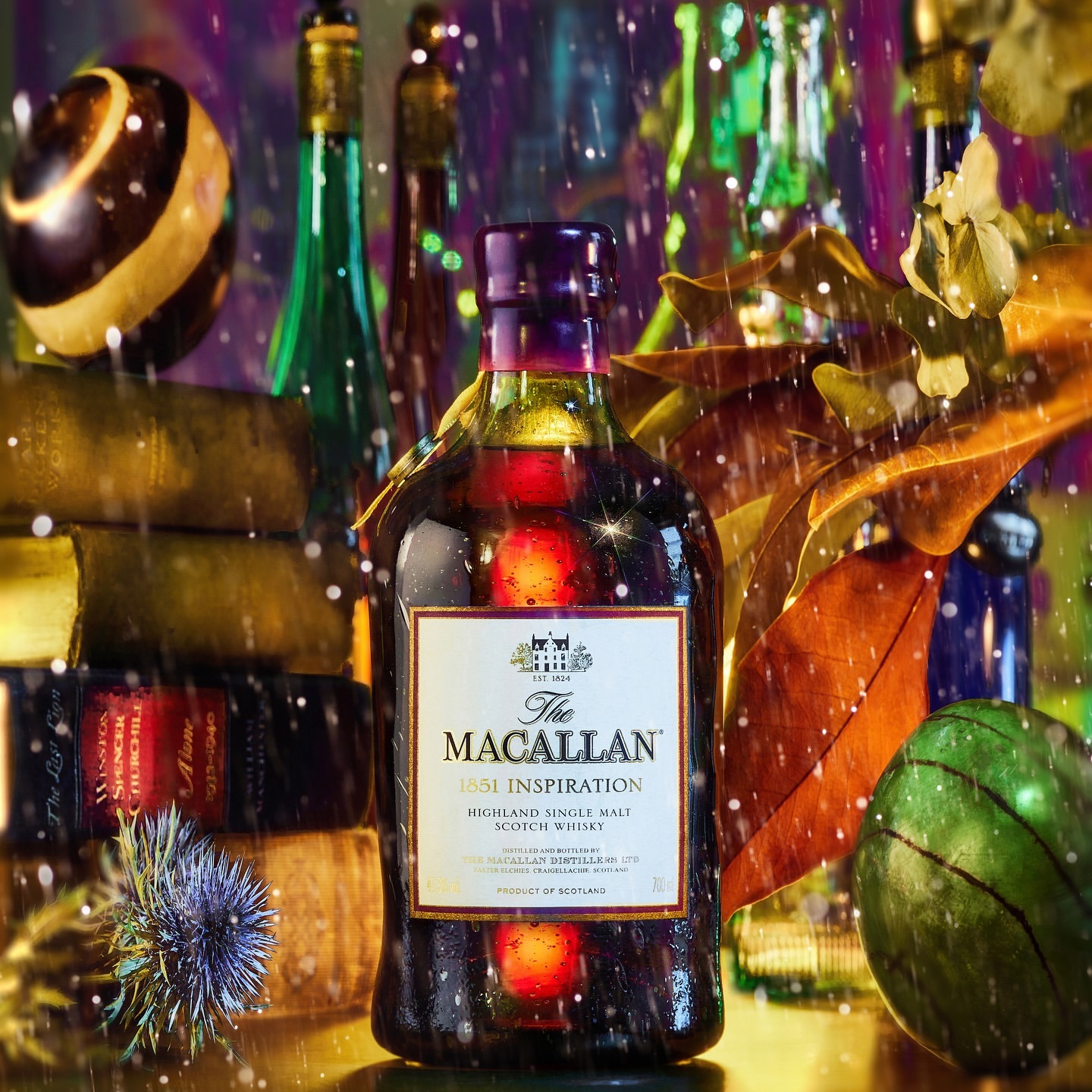 A bottle of The Macallan 1851 Inspiration single malt scotch whisky with books, decorative orbs, and autumn leaves in a vibrant still life.