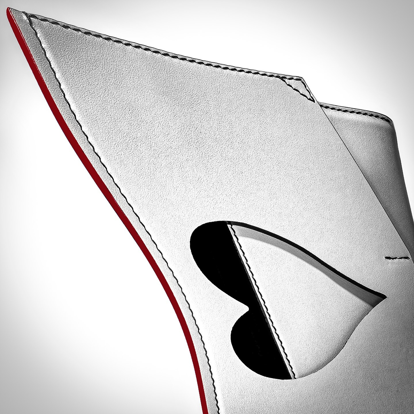 Close-up of a white leather product with a red edge, black stitching, and a heart-shaped cut-out, showcasing the product's texture and design.
