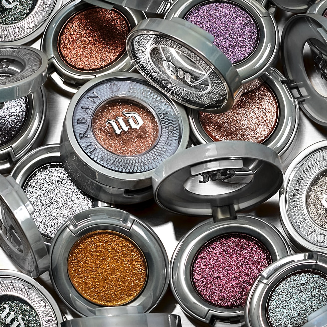 Close-up of glitter eyeshadows in round, silver compacts, arranged in a scattered pattern. Beauty product flat lay.