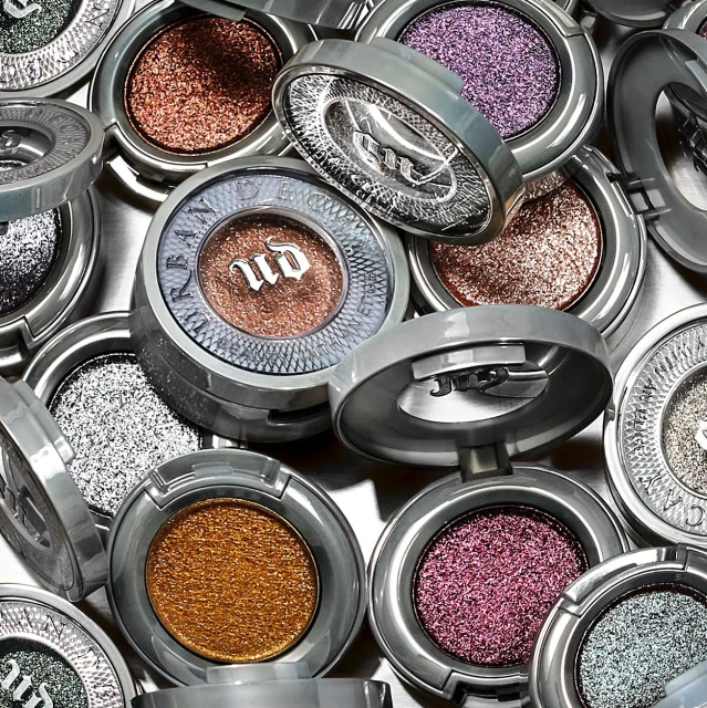 Close-up of glitter eyeshadows in round, silver compacts, arranged in a scattered pattern. Beauty product flat lay.