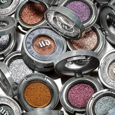 Close-up of glitter eyeshadows in round, silver compacts, arranged in a scattered pattern. Beauty product flat lay.