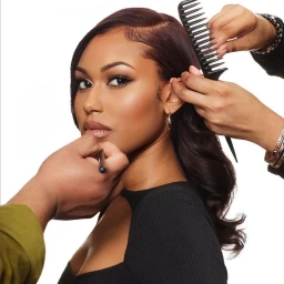 Close-up portrait of a woman receiving hair styling and makeup application against a plain white background.