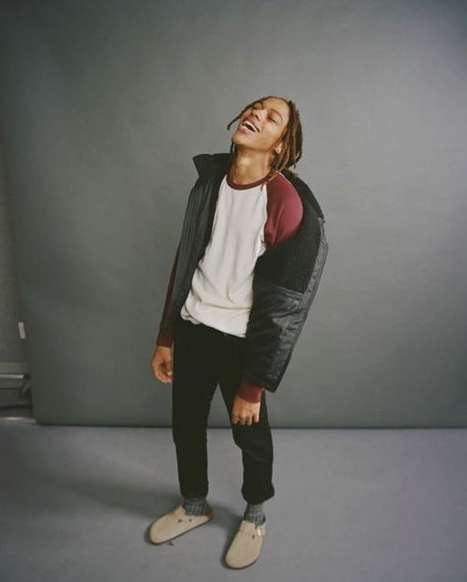 Young man with dreadlocks laughing in a ringer t-shirt and dark jacket against a grey studio backdrop