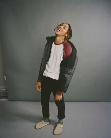 Young man with dreadlocks laughing in a ringer t-shirt and dark jacket against a grey studio backdrop
