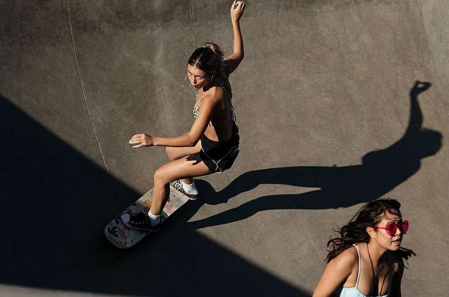 Young woman skateboarding in a concrete skatepark, with another woman watching. Outdoor skateboarding, leisure activity, sunny day.