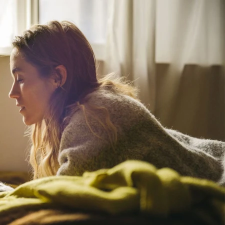 Profile of a woman with long hair lying indoors near a window wearing a textured grey knit sweater.