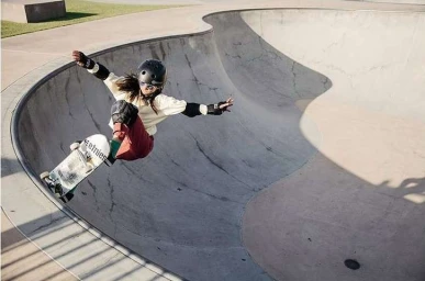 Skateboarder in a helmet dropping into a concrete bowl skatepark ramp