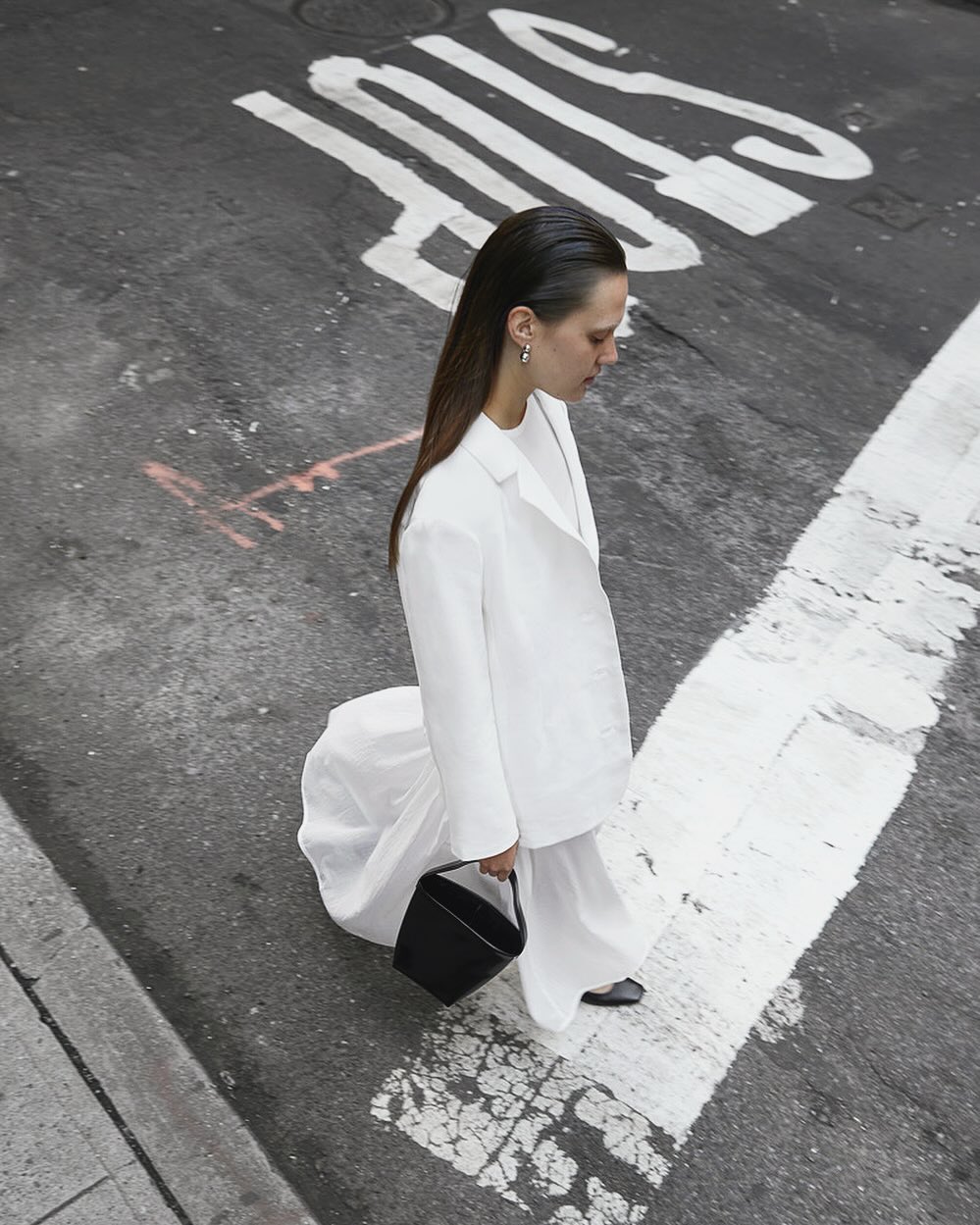 Fashion shot from above of a woman in white suit holding black purse while standing on city street with painted 'STOP' sign.