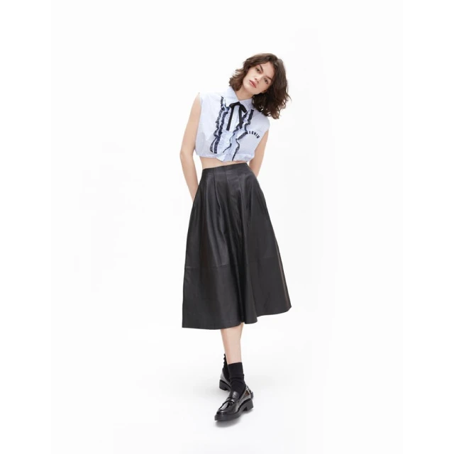 A slender woman in a light blue blouse with black ribbon detail and a black midi skirt poses in a full shot on a white background.