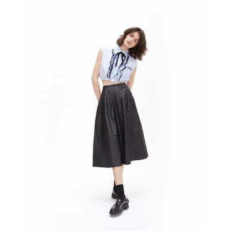 A slender woman in a light blue blouse with black ribbon detail and a black midi skirt poses in a full shot on a white background.