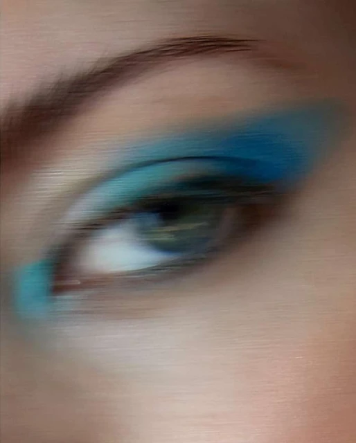 Close-up of an adult female eye with vibrant blue eyeshadow, captured with soft focus, emphasizing cosmetic beauty.