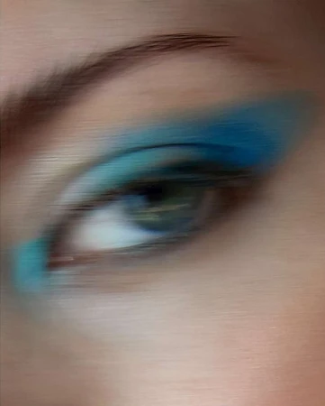 Close-up of an adult female eye with vibrant blue eyeshadow, captured with soft focus, emphasizing cosmetic beauty.