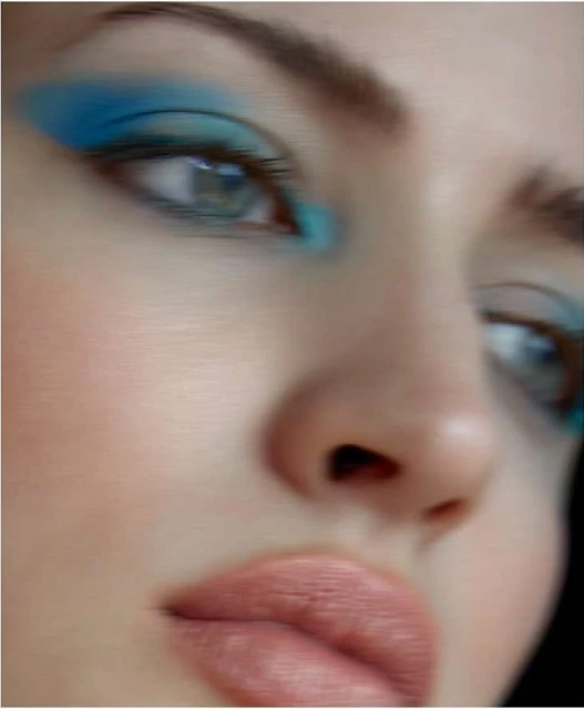 Close-up of a young woman's face featuring blue eyeshadow and light pink lips. Emphasizing facial features and makeup.