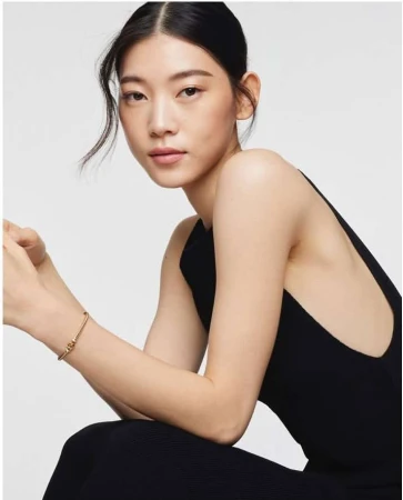 Portrait of an East Asian woman wearing a black sleeveless top and a thin gold bangle against a clean white background