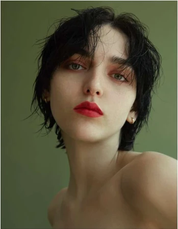 Close-up portrait of a woman with short dark wet hair, red lipstick, and an olive green background.