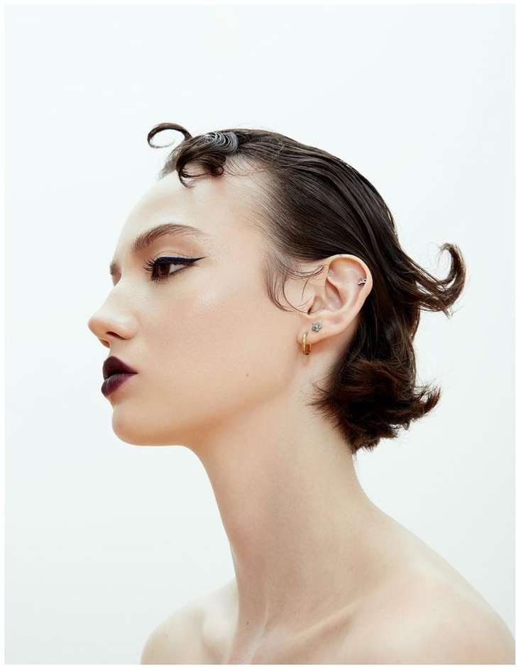 Woman with dark, short, styled hair, dark lipstick, and winged eyeliner in a studio shot against a plain white backdrop.
