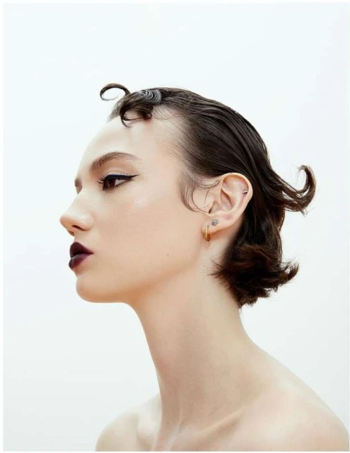 Woman with dark, short, styled hair, dark lipstick, and winged eyeliner in a studio shot against a plain white backdrop.