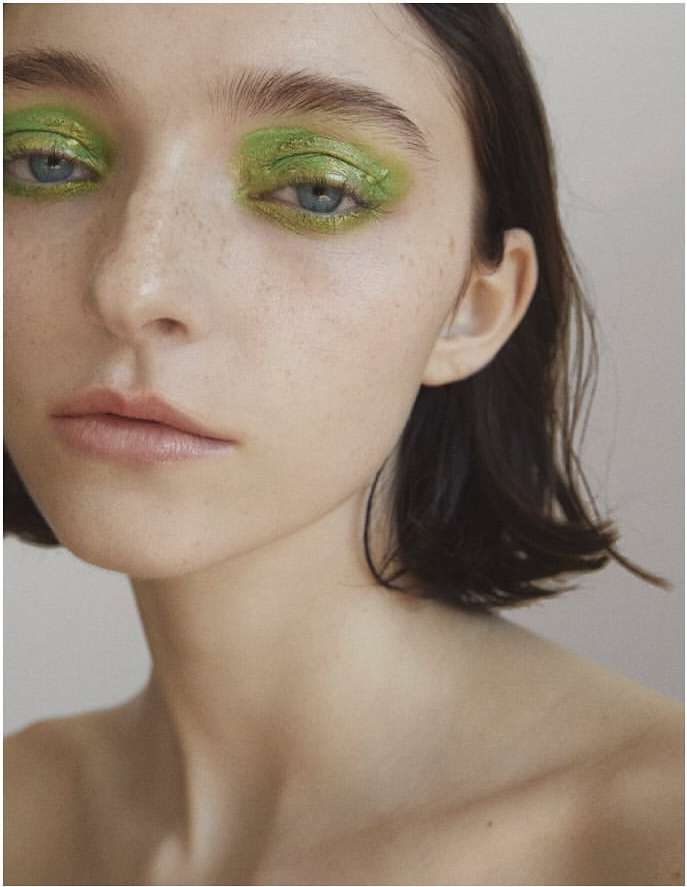 Close-up portrait of a woman with vibrant green eyeshadow and dark short hair against a neutral background by Kimber Capriotti