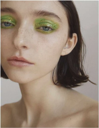 Close-up portrait of a woman with vibrant green eyeshadow and dark short hair against a neutral background by Kimber Capriotti