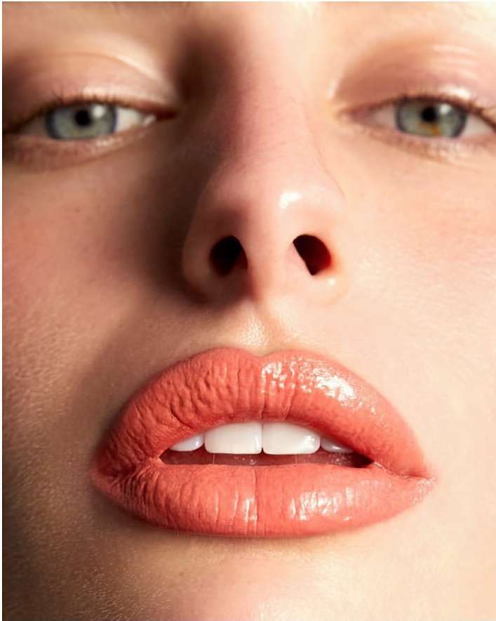 Close-up portrait focusing on glossy coral lipstick and blue eyes of a woman by photographer Kimber Capriotti.