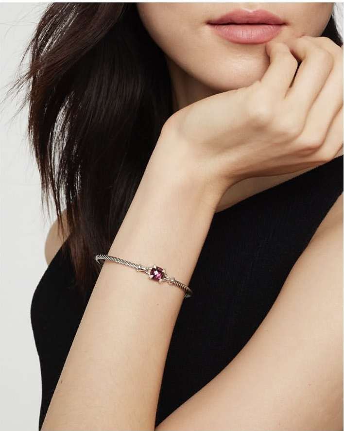 Close-up of a person wearing a silver gemstone bracelet and a black sleeveless top against a white background