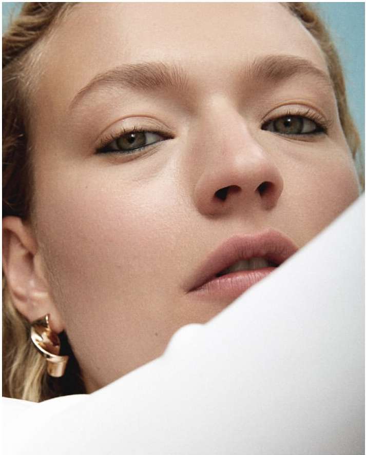 Close-up portrait of a woman with dark eyeliner and a metallic twist earring against a blue background