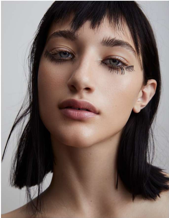 Close up portrait of a young woman with dark hair, blunt bangs, and artistic eye makeup by photographer Kimber Capriotti