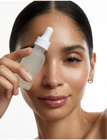 Close-up of a woman holding a translucent bottle with a dropper, skincare concept, indoor photo studio shot against a plain white backdrop.