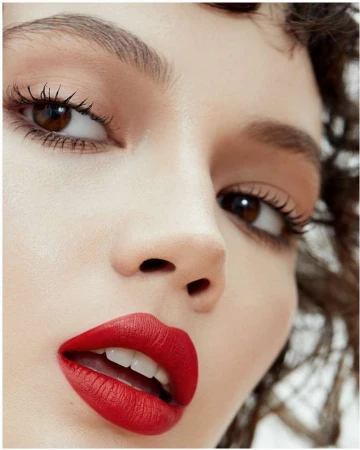 Close-up beauty portrait of a woman with bold red lipstick, dark eyeliner, and curly brown hair by Kimber Capriotti