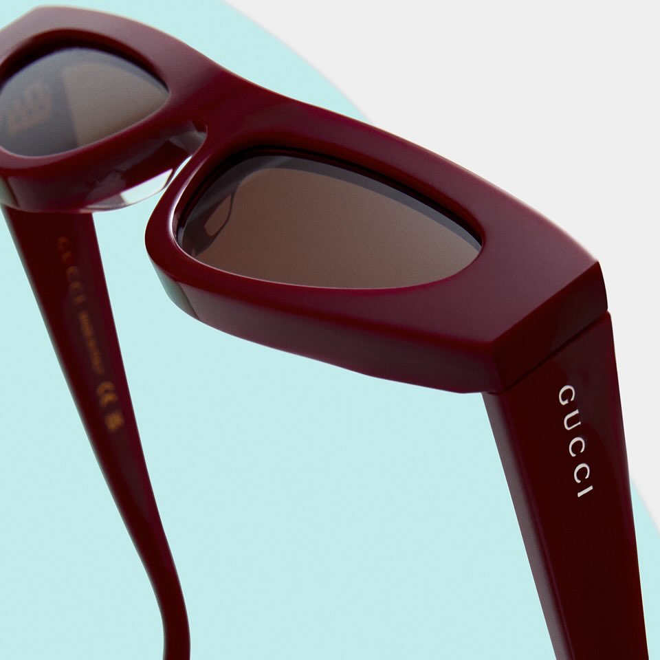 Burgundy Gucci sunglasses close-up on a blue background, showcasing a minimalist fashion eyewear style.