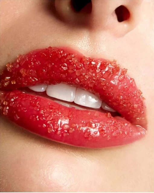Close-up of a woman's lips covered in red sugar crystals; showing teeth. The image is a beauty shot with a focus on lip detail.