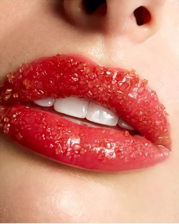 Close-up of a woman's lips covered in red sugar crystals; showing teeth. The image is a beauty shot with a focus on lip detail.