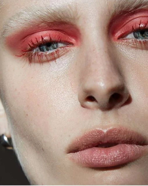 Close-up shot of a woman's face with vivid red eye makeup, light skin, and light eyebrows, creating a bold and striking beauty statement.