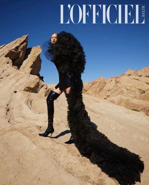 Fashion editorial featuring a woman in a black dress with a large tulle skirt posing on desert rocks under a clear blue sky.