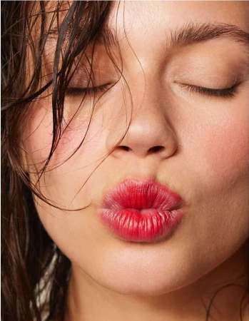 Close-up portrait of a young woman with closed eyes, pouty red lips, and wet dark hair. Beauty shot emphasizes facial features.
