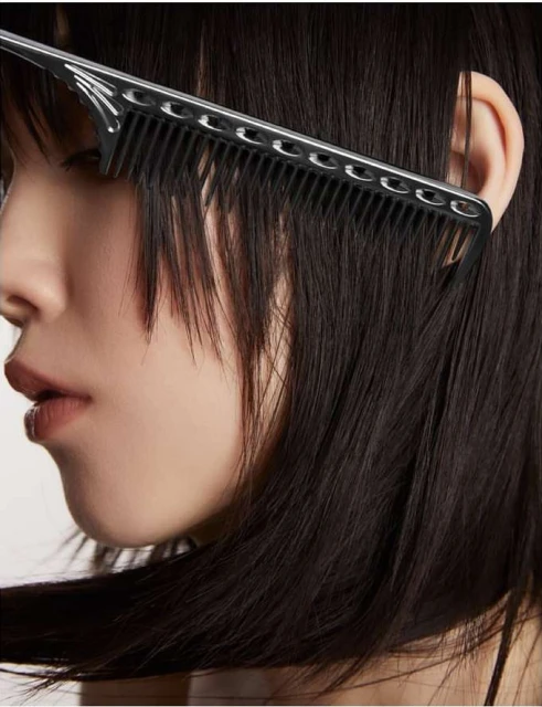 Close-up of a woman's profile with a black comb running through her dark hair, showcasing beauty and hair styling details in a studio setting.