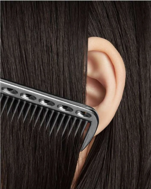 Close-up shot of an ear surrounded by dark brown hair and a black comb, likely in a salon setting for hair styling or a beauty treatment.