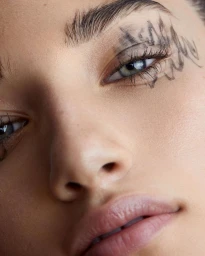 Close-up portrait of a model with artistic eye makeup and sketched markings around the eye by Kimber Capriotti