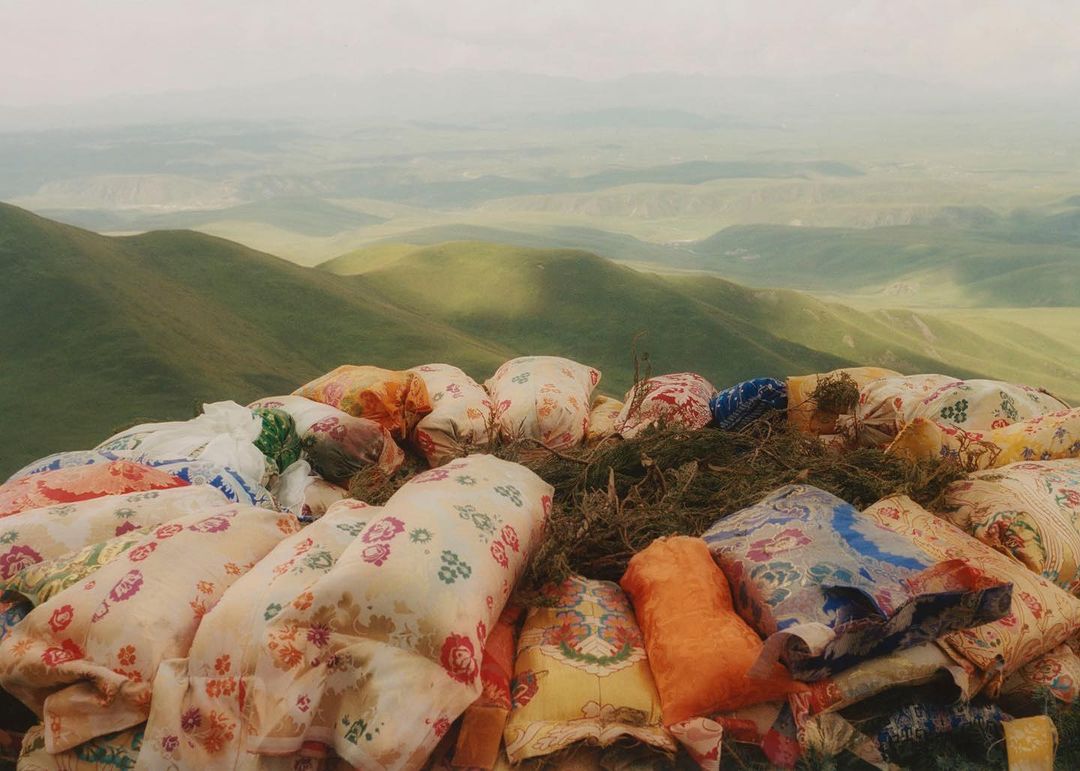Floral-patterned bundles stacked high on a hillside with lush green rolling hills and misty sky in the distance, creating a scenic view.