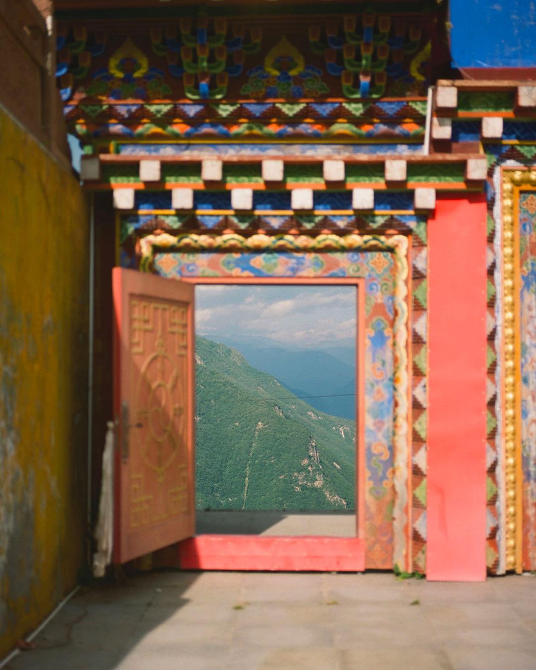 Ornate doorway frames a view of a lush mountain landscape, showcasing traditional architectural details and natural scenery in the distance.