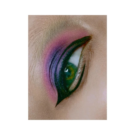 Close-up of a human eye with green iris and elaborate eye makeup in shades of pink, purple, and black for cosmetic visual.