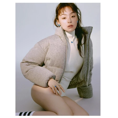 East Asian woman in a grey puffer jacket and white turtleneck posing against a white background