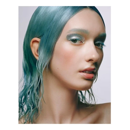 Close-up shot of a female model with blue wet-look hair and silvery eyeshadow posing against a plain backdrop in a studio setting.