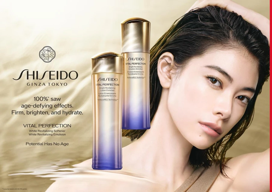 Close-up of a woman with Shiseido skincare products featuring bottles of Vital Perfection on a cream colored textured backdrop.