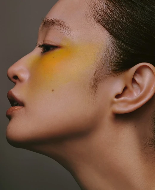 Asian adult female portrait with yellow makeup on face in profile, medium shot in photo studio against neutral gray background.