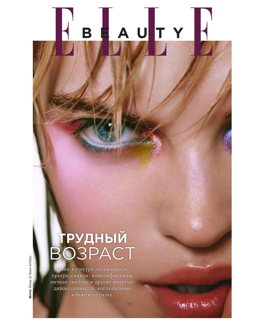 Close-up beauty shot of a woman's face on a magazine cover. She is wearing colorful makeup and has blonde hair and light skin.