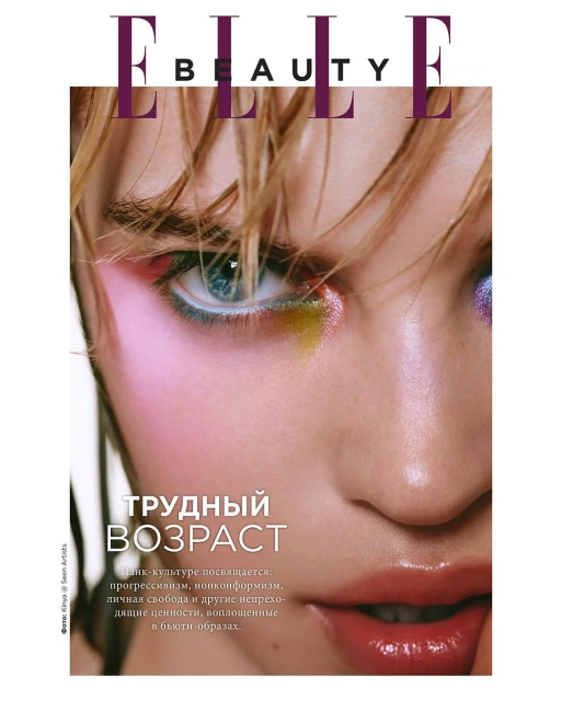 Close-up beauty shot of a woman's face on a magazine cover. She is wearing colorful makeup and has blonde hair and light skin.
