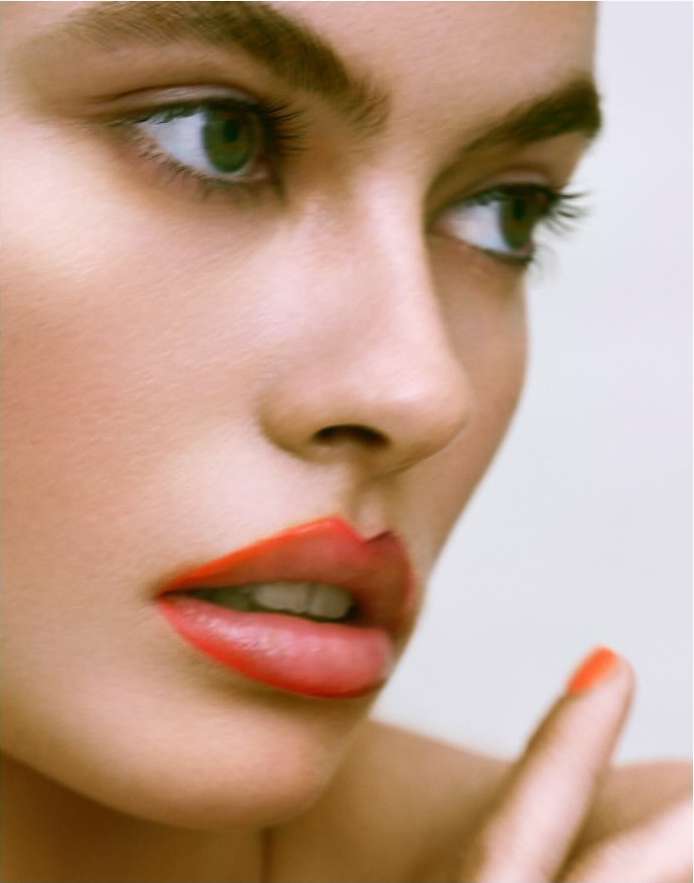 Close-up beauty shot of a woman with red lipstick and green eyes, face angled toward the upper right, and a clean, bright background.
