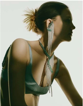 Profile portrait of a woman wearing ornate beaded earrings and a satin top against a plain light background